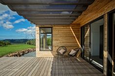 a wooden deck with two chairs on it next to a large glass door and windows