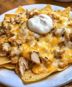 a white plate topped with nachos covered in chicken and cheese next to sour cream