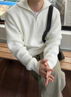 a young man sitting on a bench with his hands crossed and looking at the camera