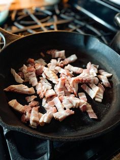 some meat is cooking in a frying pan on the stove top with other food items