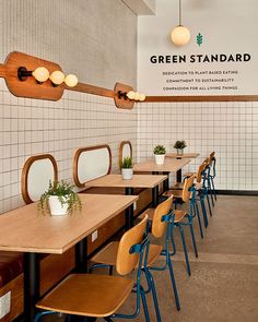 a row of wooden tables with blue chairs in front of them and a sign that reads green standard on the wall