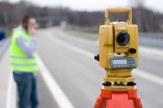 a man standing next to a road with a yellow and red camera on it's tripod