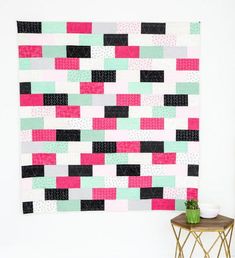 a pink, green and black wall hanging next to a small table with a potted plant on it