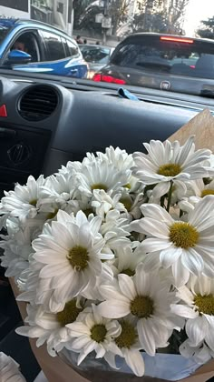 a bunch of white flowers in a vase on the dashboard of a car with other cars behind it