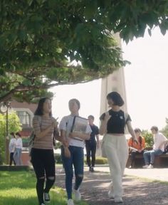 three women walking down a path in front of a tree with people sitting on benches behind them