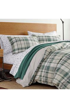 a bed with green and white plaid comforter on top of it next to a pair of shoes