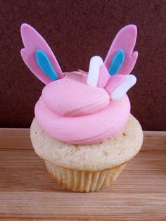 a cupcake with pink frosting and bunny ears on top is sitting on a wooden table