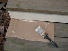 a paintbrush sitting on top of a piece of cardboard next to a wooden plank