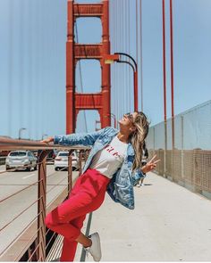 a woman leaning on a fence in front of the golden gate bridge with her arms outstretched