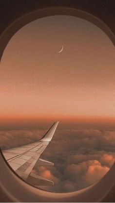 an airplane window with the view of clouds and a crescent moon in the sky above