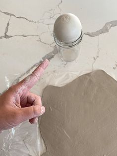 a hand pointing at a doughnut on top of a table with plastic wrap around it