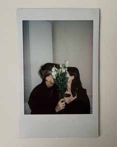 a couple kissing each other with flowers in front of them on a white frame hanging on the wall