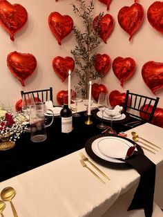 a table set for valentine's day with red heart balloons on the wall