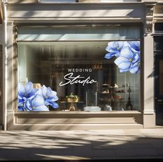 a store front window with blue flowers on the windows and white lettering reading wedding studio