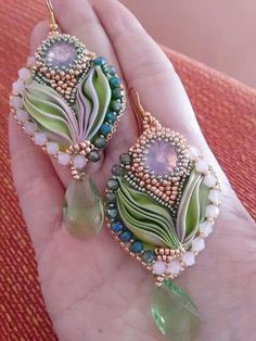 a pair of green and white beaded earrings sitting on top of a person's hand