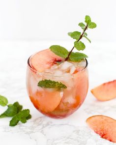 a glass filled with ice and mint garnish next to sliced peaches