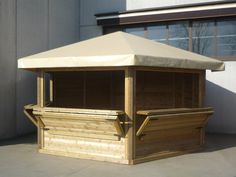 a wooden gazebo sitting on top of a cement floor next to a building with windows