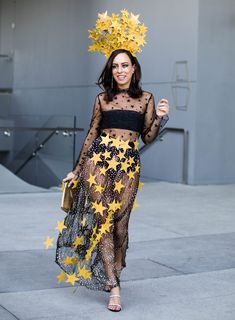 a woman in a black and yellow outfit with stars on her head walking down the street