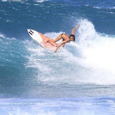 a woman riding a surfboard on top of a wave in the ocean with her arms outstretched