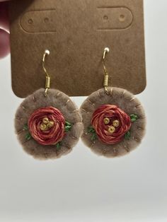 a pair of earrings with red flowers on them and gold beads hanging from the back