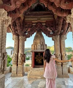 a woman in pink dress standing under an ornate structure with carvings on it's sides