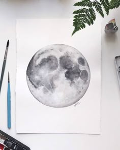 a watercolor painting of the moon with paintbrushes and other items around it