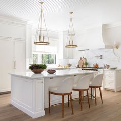 a large kitchen with white cabinets and an island in the middle is surrounded by four bar stools