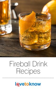 there is a glass of fireball drink with ice and oranges in the background