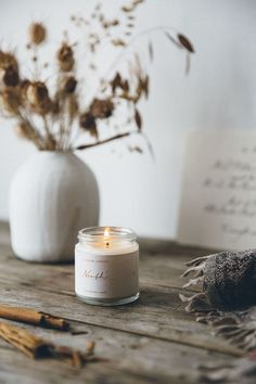 a candle sitting on top of a wooden table next to a vase with dried flowers