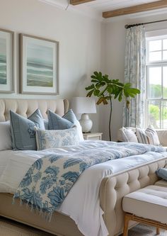 a large bed sitting in a bedroom next to a window covered in blue and white pillows