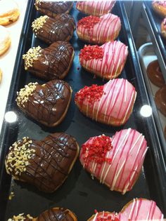 chocolate covered heart shaped donuts with sprinkles on them in a display case