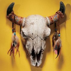 an animal's skull is adorned with feathers and beads on a yellow wall background