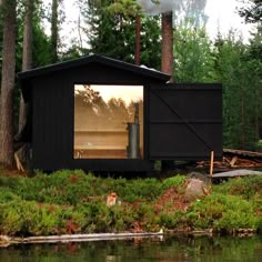 a small black cabin sitting on top of a lush green forest next to a lake