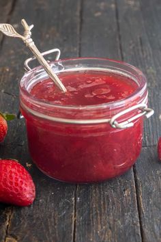 a jar filled with red liquid next to some strawberries