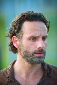 a close up of a man with a beard and blue eyes wearing a brown shirt