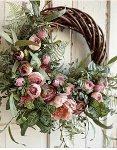 a wreath with pink flowers and greenery hanging on a door handle in front of a white wooden wall