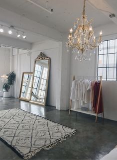 a white room with a chandelier, mirror and clothes rack in it's corner