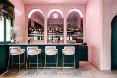 the bar is decorated in pink and green with gold barstools on either side