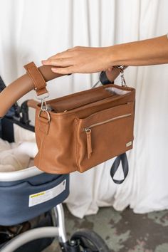 a person holding onto a brown purse in front of a stroller