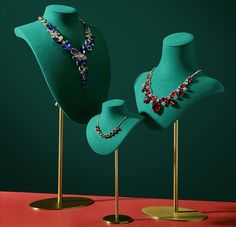 three green mannequins with necklaces on stands against a red tablecloth