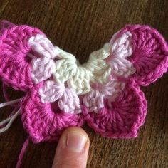 a crocheted pink and white flower being held by a person's finger