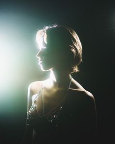 a woman in a dark room with light coming through her face and necklaces around her neck