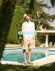 a man standing in front of a swimming pool wearing sandals and a white cardigan