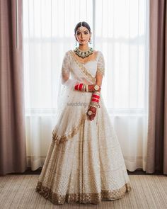 a woman standing in front of a window wearing a bridal outfit