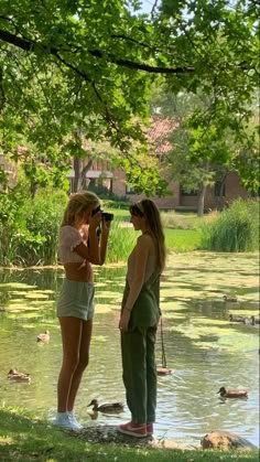 two women are standing in the water and one is holding a camera to take pictures