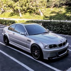 a silver car parked in a parking lot next to some bushes and trees on the side of the road