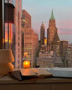 an open book sitting on top of a window sill next to a cup and lamp