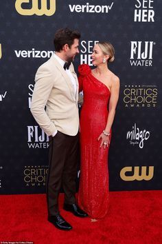 a man and woman in formal wear standing on the red carpet at an awards event