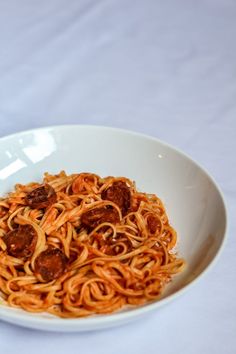 a white bowl filled with spaghetti and meatballs on top of a tablecloth covered table