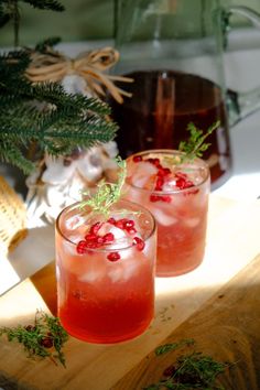 two glasses filled with drinks sitting on top of a cutting board next to a pine tree